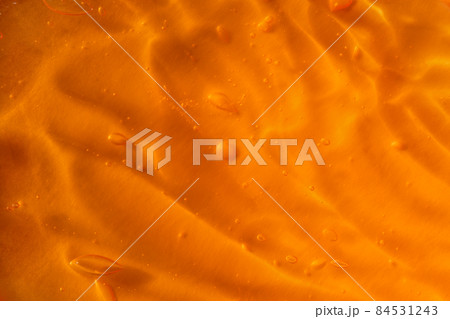 Texture of transparent yellow gel with air bubbles and waves on orange background. Concept of skin moisturizing, body care and prevention of covid19. Liquid beauty product closeup. Backdrop, flat lay 84531243