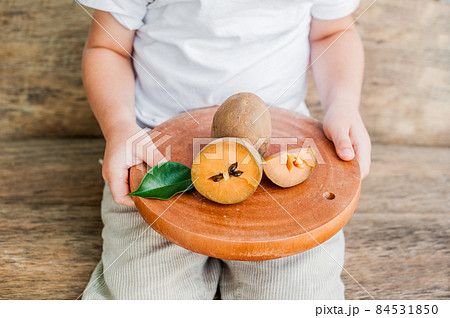 Hands holding a board with fresh sapodilla fruits on old wooden background 84531850