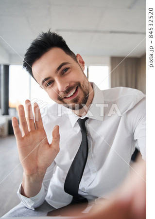 Businessman wearing formal clothes greeting with somebody while waving 84532520