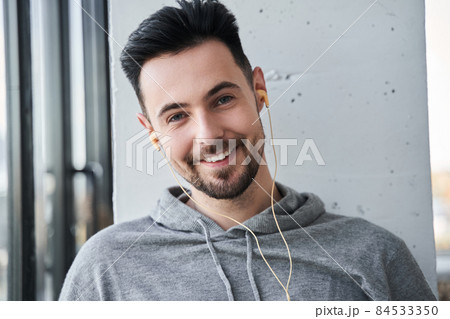Man wearing earphones looking at the camera with happy smile while listening music at home 84533350