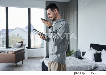 Male spending time in bedroom with smartphone while recording voice message Male spending time in bedroom with smartphone while recording voice message 84533380