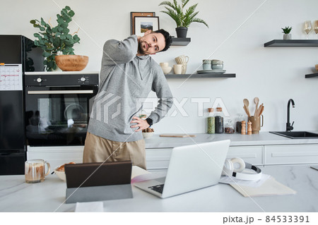 Man doing a warm-up during the working at the laptop while standing at the kitchen 84533391