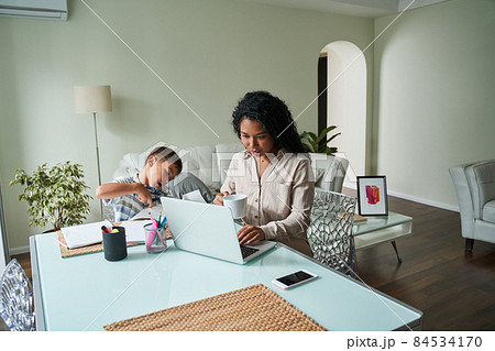 Black mother using laptop and child crafting 84534170
