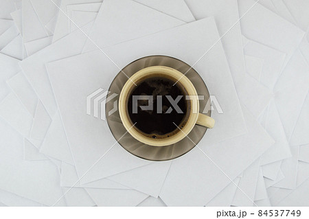 short break at the hard worker: a Cup of hot coffee and a brown glass saucer on a disorderly stack of papers 84537749