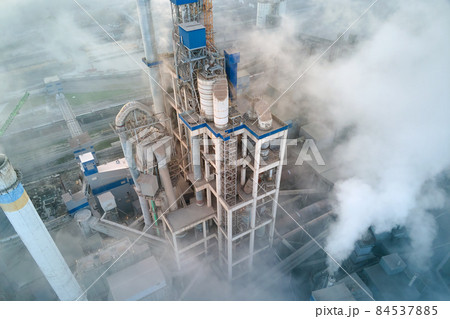 Aerial view of cement factory with high concrete plant structure and tower crane at industrial manufacturing site on foggy evening. Production and global industry concept. Aerial view of cement factory with high concrete plant structure and tower crane at industrial manufacturing site on foggy evening. Production and global industry concept. 84537885