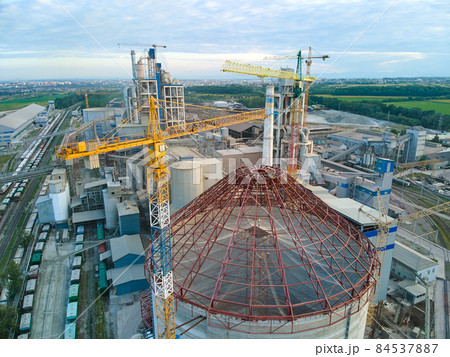 Aerial view of cement factory under construction with high concrete plant structure and tower cranes at industrial production area. Manufacture and global industry concept. Aerial view of cement factory under construction with high concrete plant structure and tower cranes at industrial production area. Manufacture and global industry concept. 84537887
