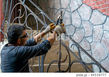 Man is holding welding machine in hands, preparing to start work on welding metal parts to stair railing in private house. 84539777