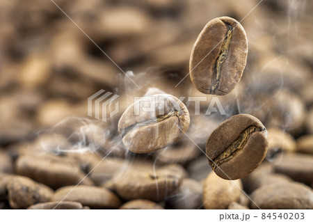 Flying fresh coffee beans as a background with copy space. Coffee beans falling down with white steam vapour. Flying fresh coffee beans as a background with copy space. Coffee beans falling down with white steam vapour. 84540203