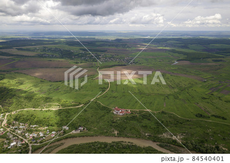 Aerial view of town or village with rows of buildings and curvy streets between green fields in summer. Countryside landscape from above. Aerial view of town or village with rows of buildings and curvy streets between green fields in summer. Countryside landscape from above. 84540401