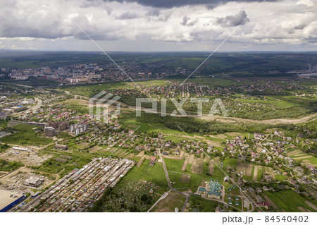 Aerial view of town or village with rows of buildings and curvy streets between green fields in summer. Countryside landscape from above. 84540402