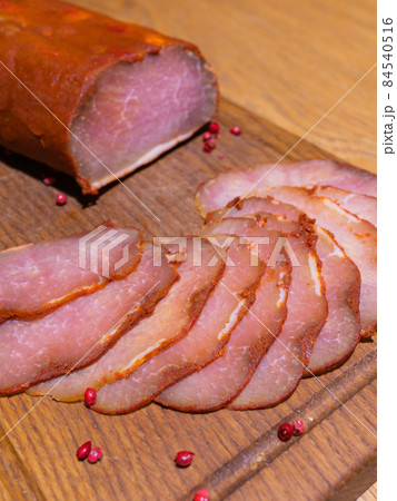 Sliced smoked gammon on a wooden table with addition of fresh herbs and aromatic spices. 84540516