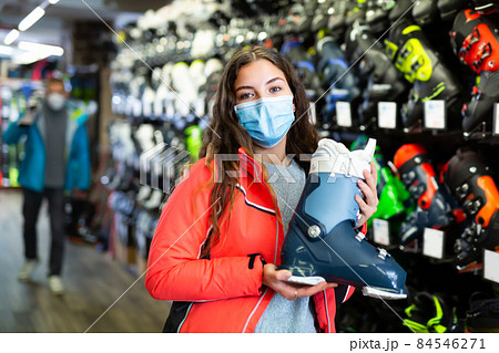 Customer woman in protective mask is choosing boots for skiing in store 84546271