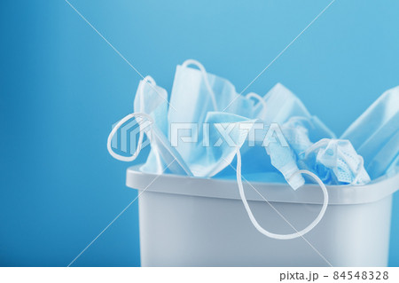 A white trash can full of virus protection masks on a blue background. 84548328
