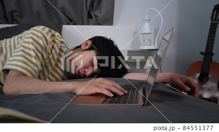 Tired young asian man sleeping on bed near computer laptop. 84551377
