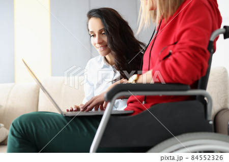 Best friends spend time together watching movie on laptop, woman in wheelchair hold device on lap Best friends spend time together watching movie on laptop, woman in wheelchair hold device on lap 84552326