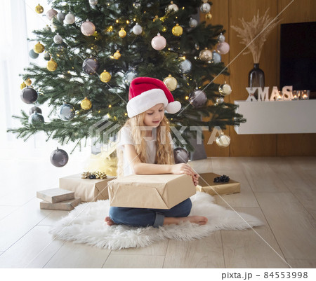 A girl with gifts plays near the Christmas tree. 84553998