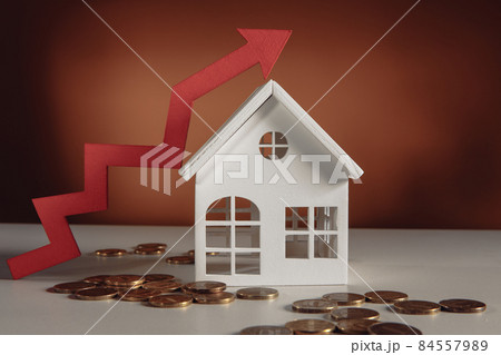 Coins on a table, a red up arrow and house. The concept of the rising price of real estate Coins on a table, a red up arrow and house. The concept of the rising price of real estate 84557989