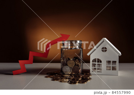 Glass jar filled coins, a red up arrow and house. The concept of the rising price of real estate Glass jar filled coins, a red up arrow and house. The concept of the rising price of real estate 84557990