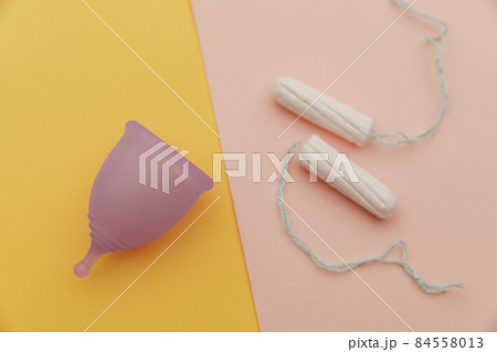Menstrual cup and tampons on a yellow pink background. Concept of women's healthcare and hygiene Menstrual cup and tampons on a yellow pink background. Concept of women's healthcare and hygiene 84558013