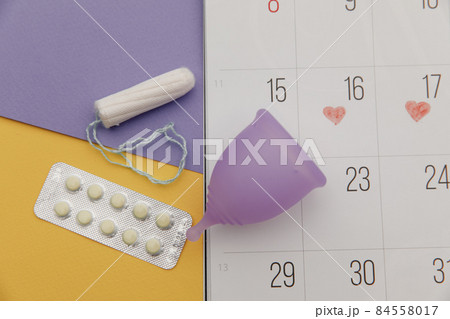 Calendar, tampon and menstrual cup with pain relief pills close-up. Woman critical days and hygiene protection 84558017