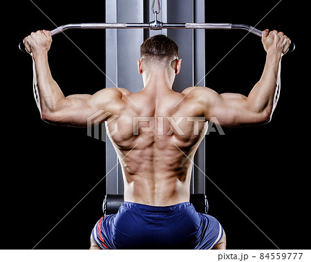 Back view of young topless bodybuilder works out pulling down on cable machine in gym 84559777