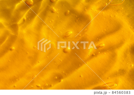 Texture of transparent yellow gel with air bubbles and waves on orange background. Concept of skin moisturizing, body care and prevention of covid19. Liquid beauty product closeup. Backdrop, flat lay 84560383