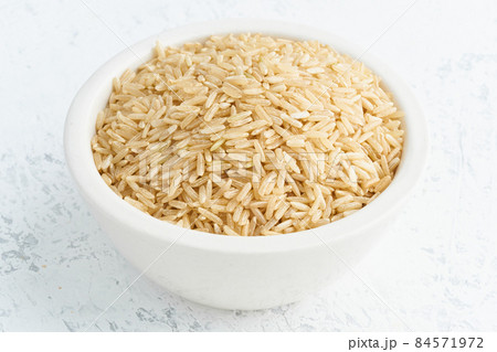 Brown rice in white bowl on white background. Dried cereals in cup, 84571972