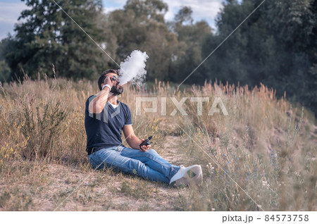 Handsome man vaping and releases a cloud of vapor. Modern ways of quitting tobacco. Handsome man vaping and releases a cloud of vapor. Modern ways of quitting tobacco. 84573758