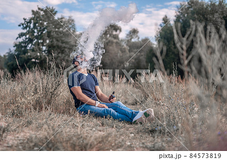 Stylish vape man smokes e-cigarette exhales smoke on the ground. Smoking cessation tobacco. Stylish vape man smokes e-cigarette exhales smoke on the ground. Smoking cessation tobacco. 84573819