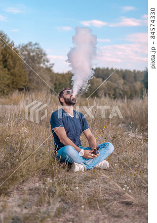 Stylish brutal man smoking an vape on the forest floor. Health concept. 84574330