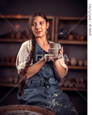 Pottery girl shows the finished clay product in the pottery workshop. Handicraft production. 84575781