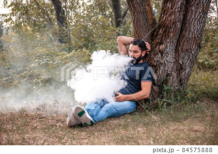 Stylish bearded smoker blows up a couple an electronic cigarette outside. Modern ways of quitting tobacco. Stylish bearded smoker blows up a couple an electronic cigarette outside. Modern ways of quitting tobacco. 84575888