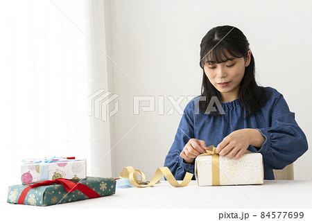 ラッピングしたプレゼントにリボンをかける女性 84577699