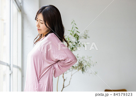 部屋着を着てリビングの窓際に立つ体調不良の女性 84579323