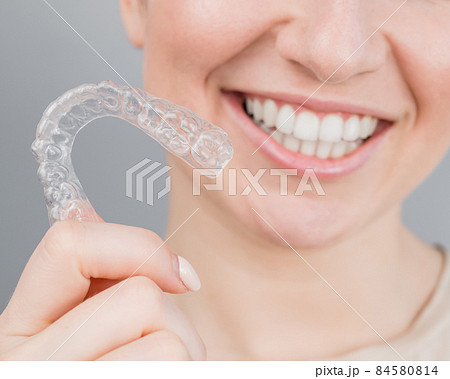 Close-up portrait of a woman putting on a transparent plastic retainer. A girl corrects a bite with the help of an orthodontic device Close-up portrait of a woman putting on a transparent plastic retainer. A girl corrects a bite with the help of an orthodontic device 84580814