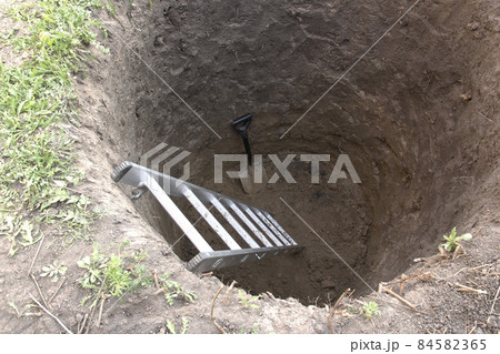 Deep pit in the ground. In the pit shovel and ladder. Digging a hole. Deep pit in the ground. In the pit shovel and ladder. Digging a hole. 84582365