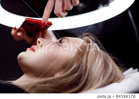 Cosmetologist making photo of work on mobile phone red permanent make up tattoo on young woman lips Cosmetologist making photo of work on mobile phone red permanent make up tattoo on young woman lips 84586176