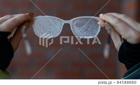 A woman holds frozen glasses covered with frost on the background of a brick wall A woman holds frozen glasses covered with frost on the background of a brick wall 84588660