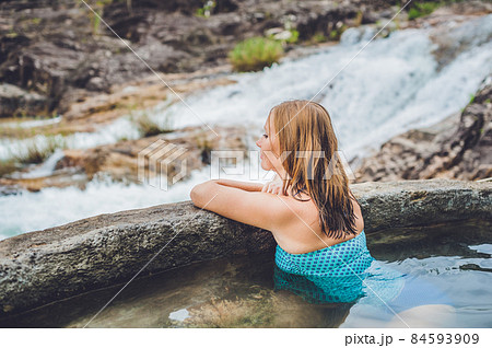 Geothermal spa. Woman relaxing in hot spring pool against the background of a waterfall 84593909