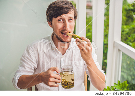 Cane sugar concept. The man jokingly eating sugar cane and drinks tea Cane sugar concept. The man jokingly eating sugar cane and drinks tea 84594786