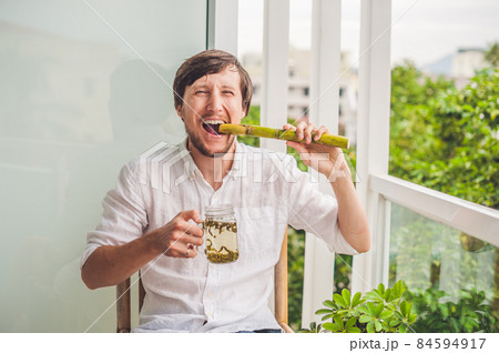 Cane sugar concept. The man jokingly eating sugar cane and drinks tea Cane sugar concept. The man jokingly eating sugar cane and drinks tea 84594917