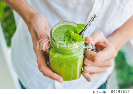 Mason jar mugs filled with green spinach, banana and coconut milk health smoothie with with a spoon of oatmeal In hands on wooden rustic table Mason jar mugs filled with green spinach, banana and coconut milk health smoothie with with a spoon of oatmeal In hands on wooden rustic table 84595617