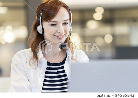 パソコンに向かって話すヘッドセットをつけた外国人女性　 84595942