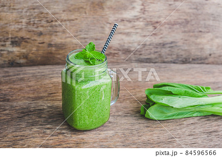 Mason jar mugs filled with green spinach, banana and coconut milk health smoothie with with a spoon of oatmeal on wooden rustic table 84596566