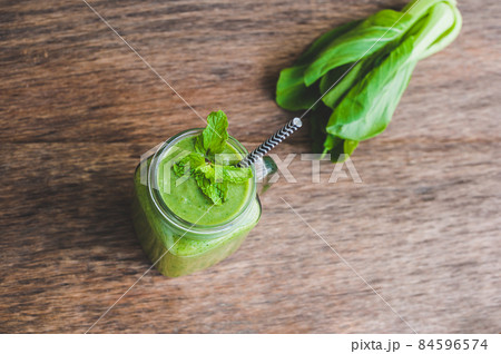 Mason jar mugs filled with green spinach, banana and coconut milk health smoothie with with a spoon of oatmeal on wooden rustic table 84596574