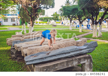Cute blond boy climbs up the stone blocks on the playground. Childhood, concept 84598241