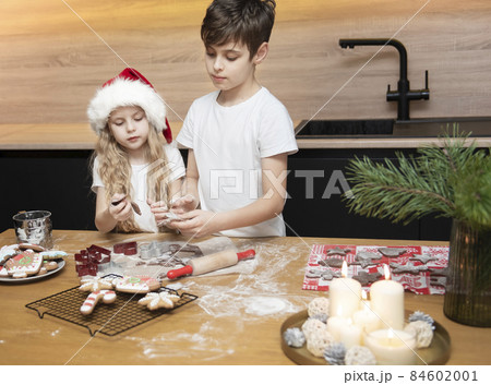 Children - a boy and a girl are preparing gingerbread in the kitchen Children - a boy and a girl are preparing gingerbread in the kitchen 84602001