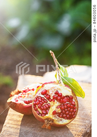 Ripe organic broken pomegranate, cut in half on wooden background. Selective focus, natural green bokeh with sunlight . Ripe organic broken pomegranate, cut in half on wooden background. Selective focus, natural green bokeh with sunlight . 84603056