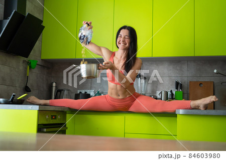Flexible woman cooking in the kitchen. Concept of healthy lifestyle, yoga and wellness Flexible woman cooking in the kitchen. Concept of healthy lifestyle, yoga and wellness 84603980