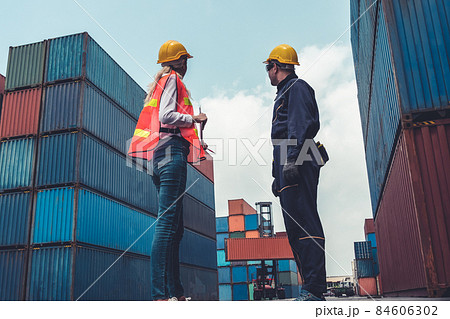Industrial worker works with co-worker at overseas shipping container yard Industrial worker works with co-worker at overseas shipping container yard 84606302